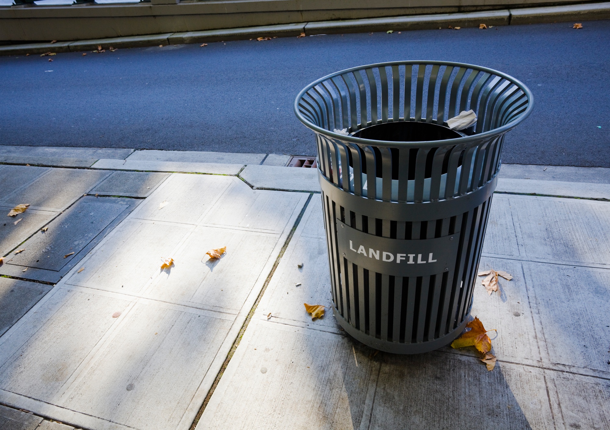 A garbage can on the sidewalk in the city.